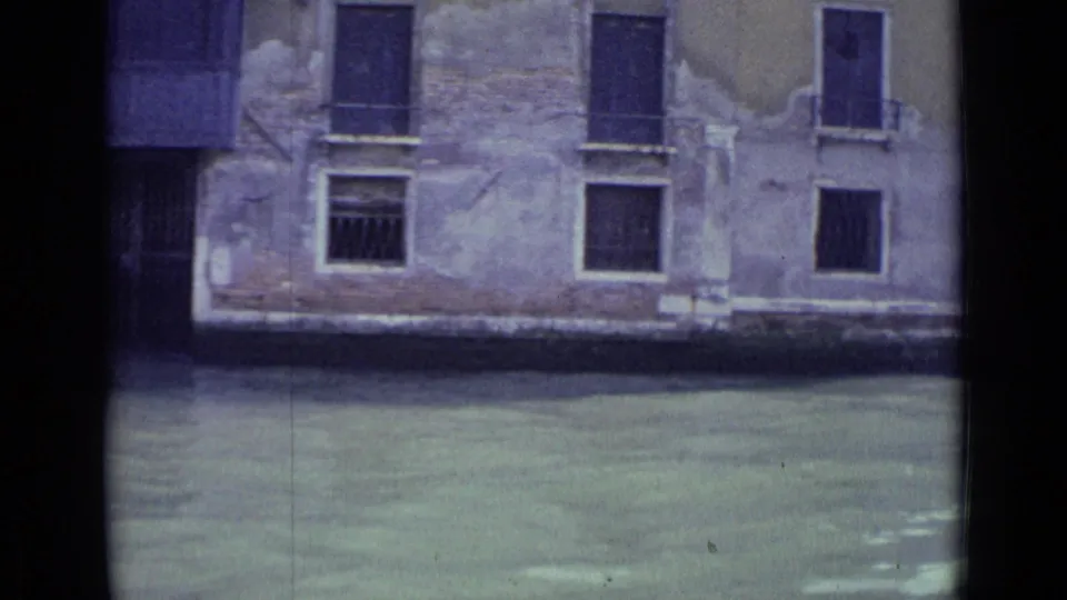 1962 Venice canal view from a boat, showing greenish water below a worn plaster facade with shuttered and barred windows.