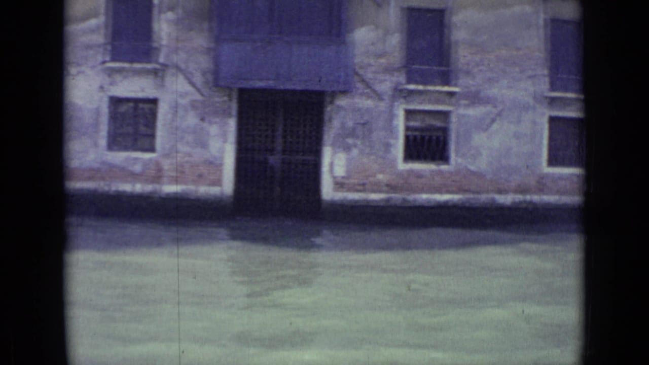 Flooded canal edge with a dark doorway and shuttered windows on an old facade.