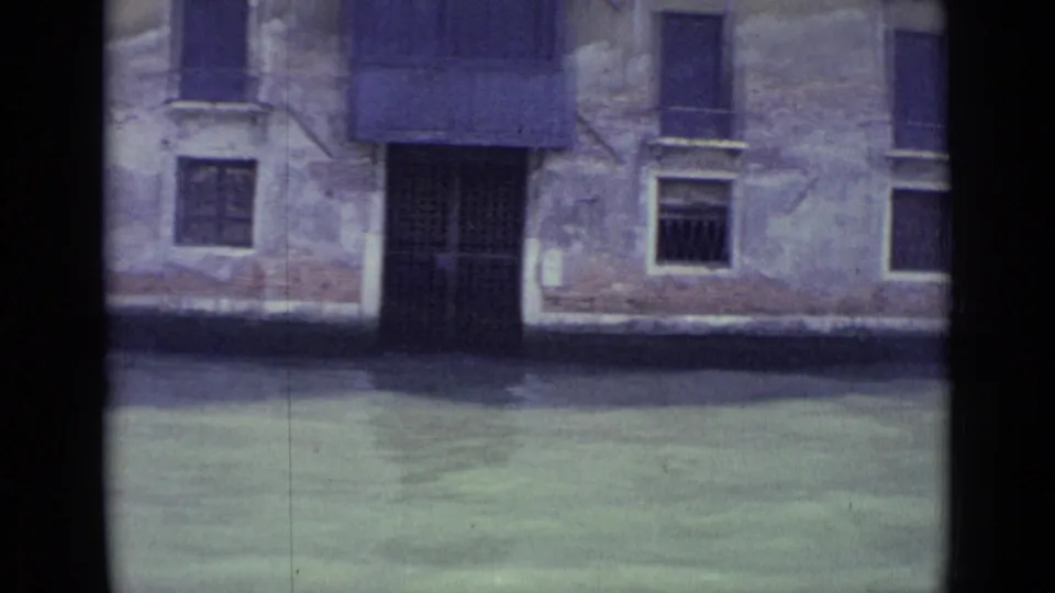 1962 Venice boat view of water against an aged building facade with a dark central doorway, shutters, and worn plaster.