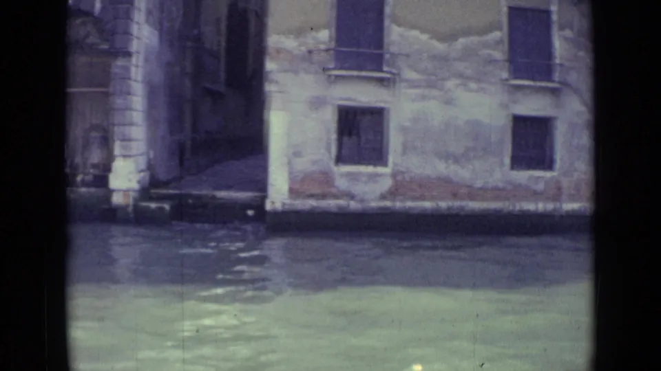 1962 Venice boat-level view of a narrow passage or bridge opening beside weathered canal-facing buildings and shuttered windows.