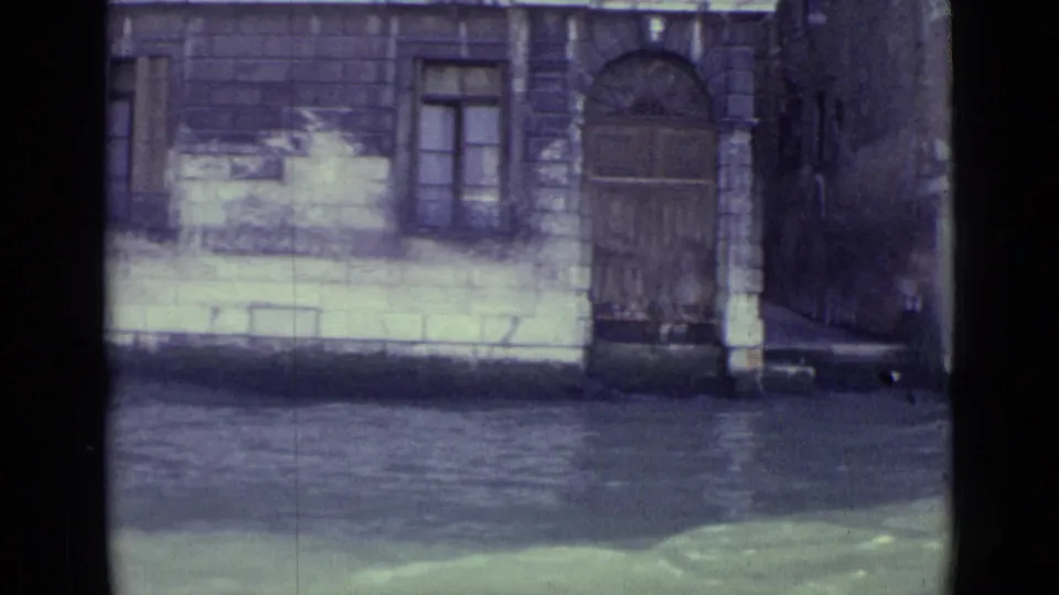 Venice canal view from the stated 1962 home movie, showing a stone facade, arched doorway, windows and rippling water.