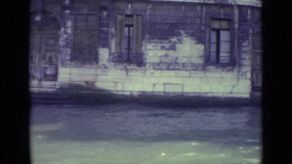 1962 Venice canal frame with a weathered waterfront wall, arched entrance, barred windows and water in the foreground.