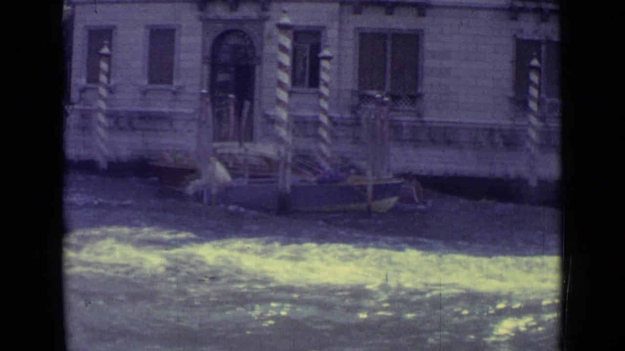 Canal water in front of a stone building with striped mooring poles.