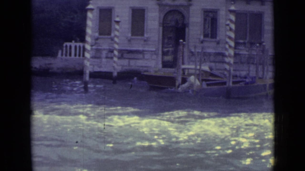 Stone canal facade with striped mooring poles beside rippling water.