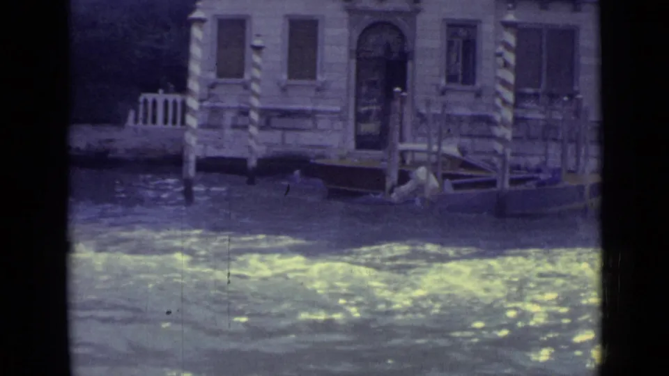 Venice canal frontage in 1962, showing bright water reflections, stone architecture, and striped mooring posts.