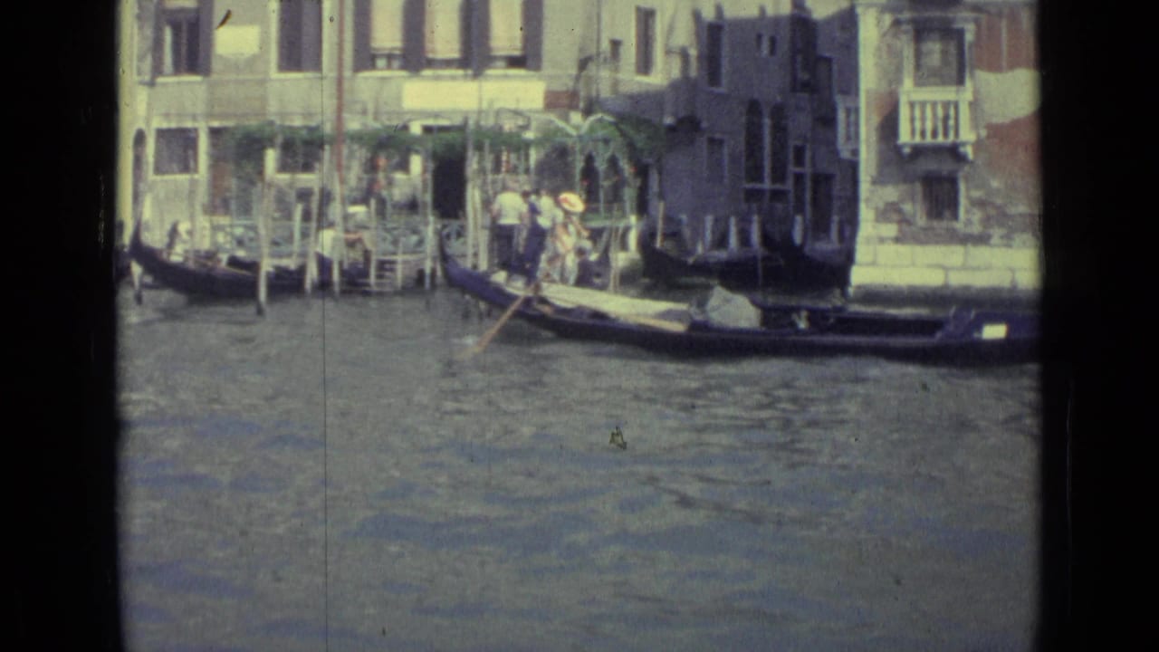 Gondola with passengers beside Venetian canal buildings and mooring poles.
