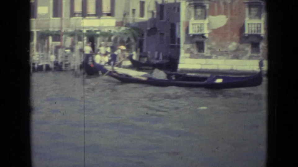 1962 Venice home-movie frame showing a gondola on canal water near historic facades and small balconies.