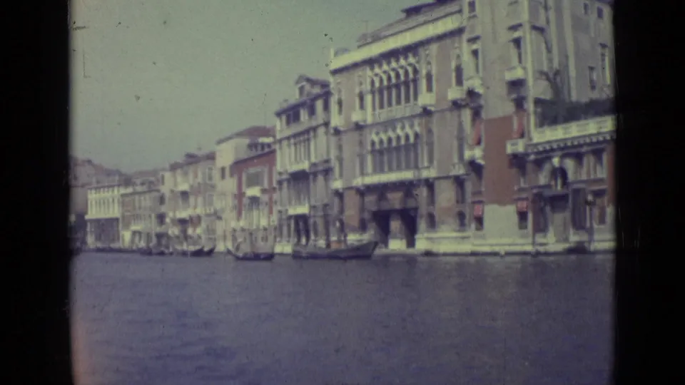 1962 Venice canal scene with rows of waterfront buildings, moored boats, and open water seen from a visitor perspective.