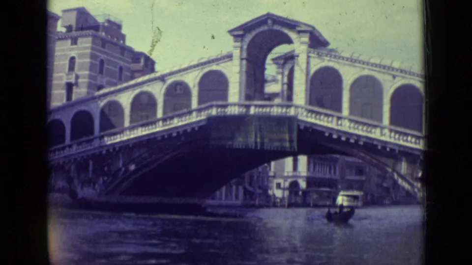 1962 Venice frame showing the Rialto Bridge over canal water, with arched stonework, nearby buildings, and boats below.