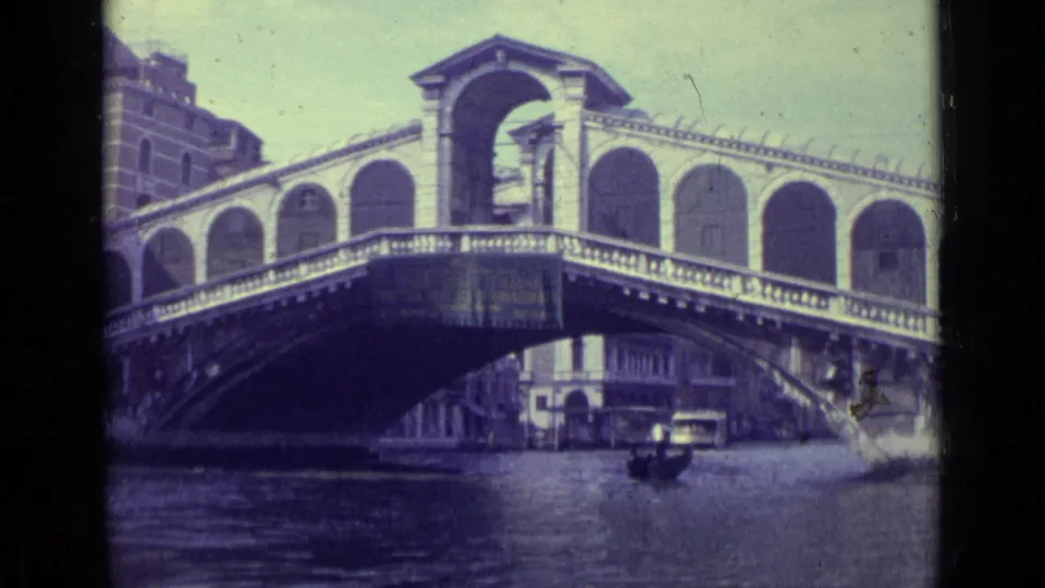 1962 8mm view of Venice's Rialto Bridge spanning a canal, with a gondola below and historic buildings along the water.