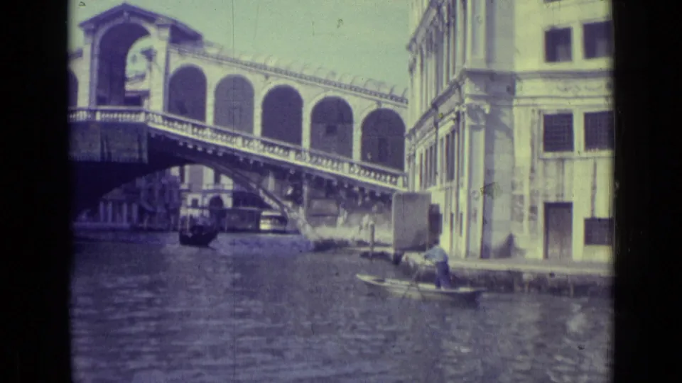 1962 Venice home-movie frame showing the Rialto Bridge, canal water, waterfront buildings, and a gondola near the right bank.