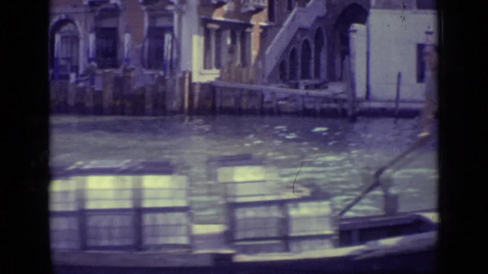 Venice canal scene with a low boat carrying stacked crates, mooring posts, and arched building details along the water.