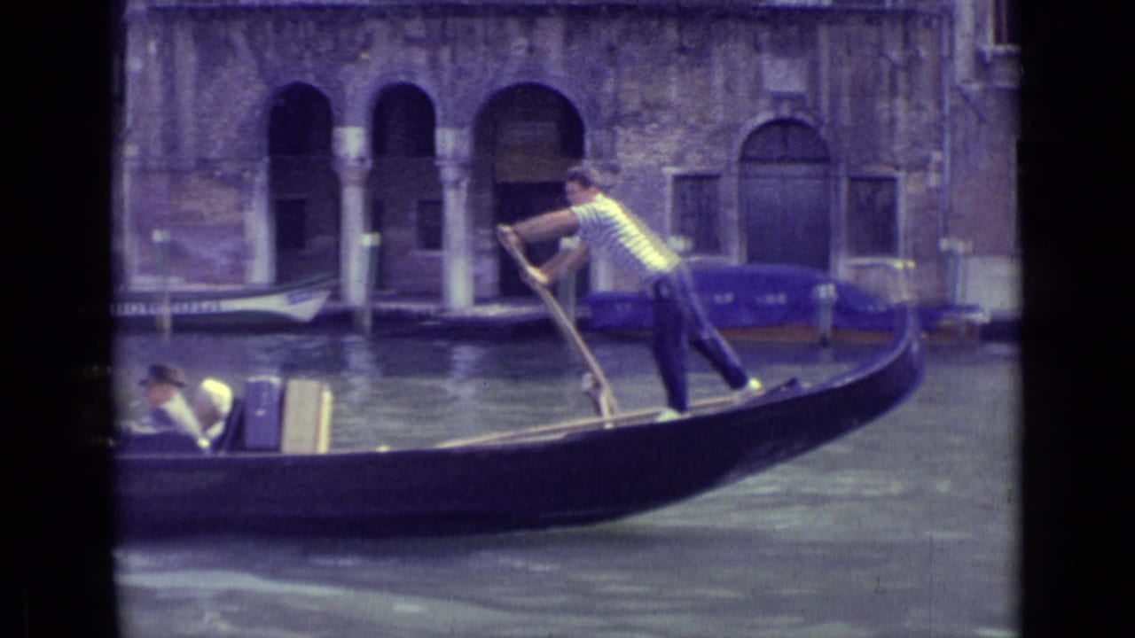 Gondolier rows a dark gondola with passengers along a canal beside arched buildings.