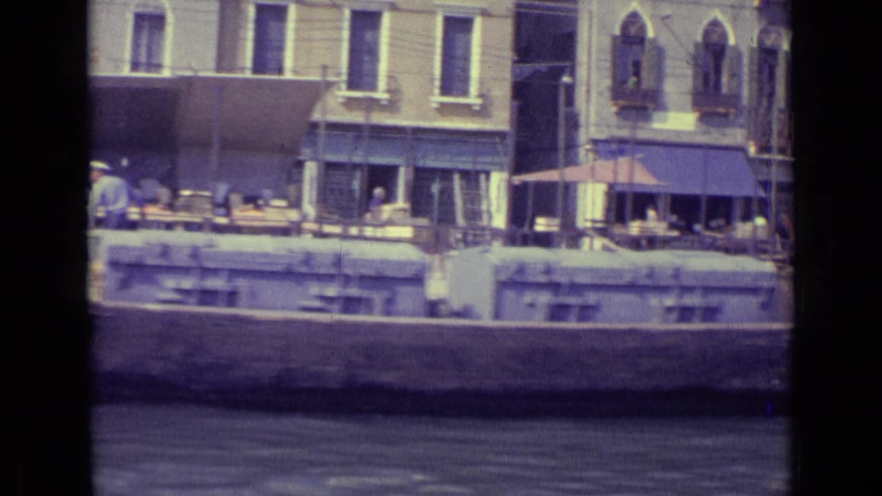 Canal-side buildings with awnings, cafe tables, and a moored boat across the water.