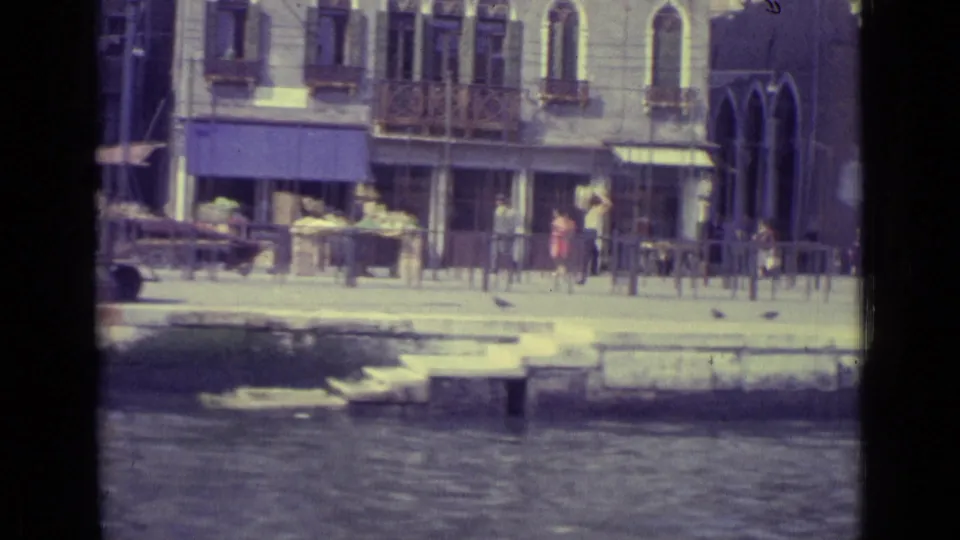 1962 Venice canal-side view with pedestrians, cafe seating, stone steps, awnings, and arched building details.