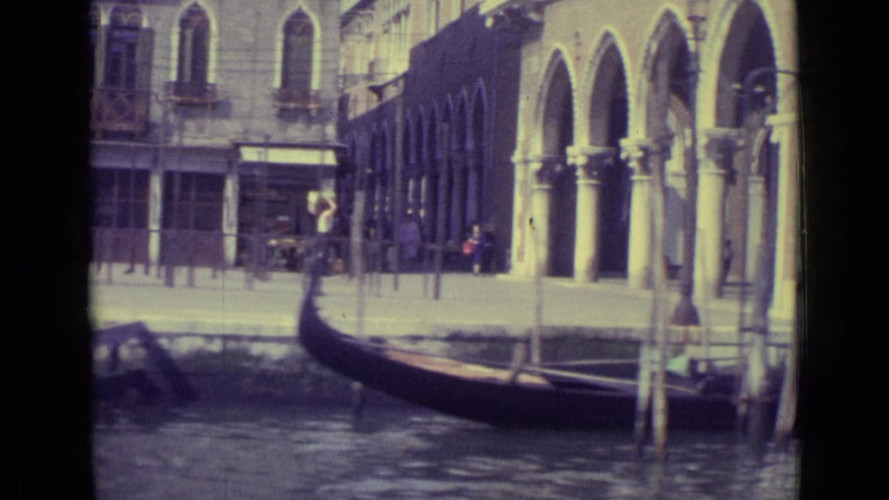 Gondola on a Venice canal beside arched waterfront buildings and mooring poles.