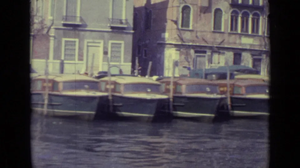 1962 Venice home-movie view of several small motorboats moored along canal water before shuttered waterfront buildings.