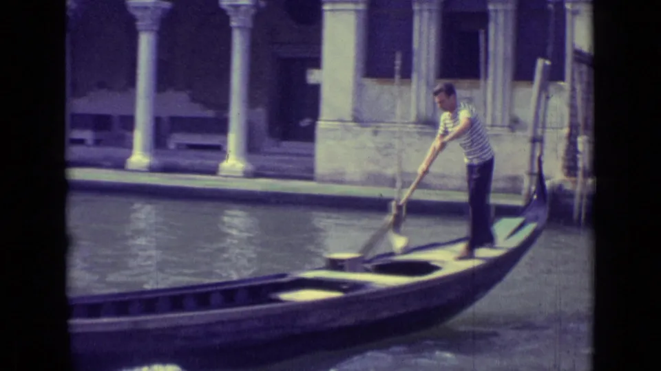 1962 Venice frame showing a gondolier standing on a gondola with a long oar beside canal-side columns.