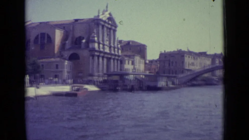 1962 Venice home-movie frame showing a broad canal view, a large historic building, and a bridge in the distance.