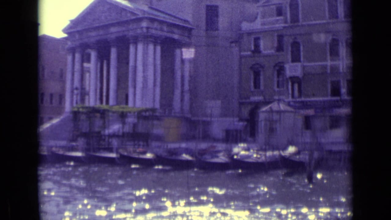 Venetian canal with moored boats, sunlit water, and a columned building beside older facades.