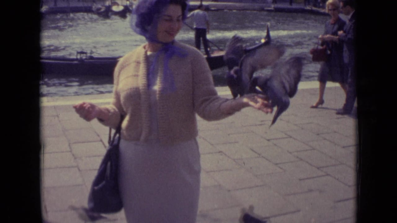 Woman in a purple headscarf feeding pigeons beside a canal with gondolas behind her.