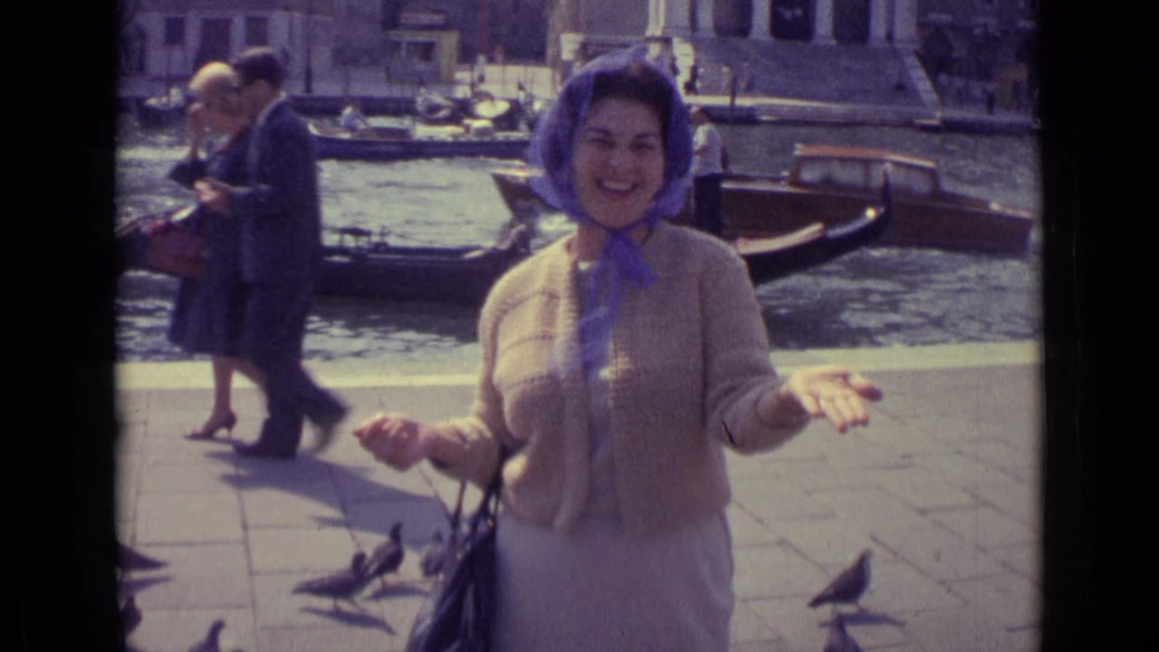 Woman in a headscarf smiles near a canal as pigeons stand on the pavement.
