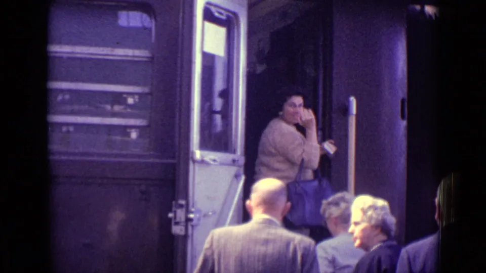 A woman in the train doorway appears to wave or gesture as passengers wait on the Venice platform in 1962.