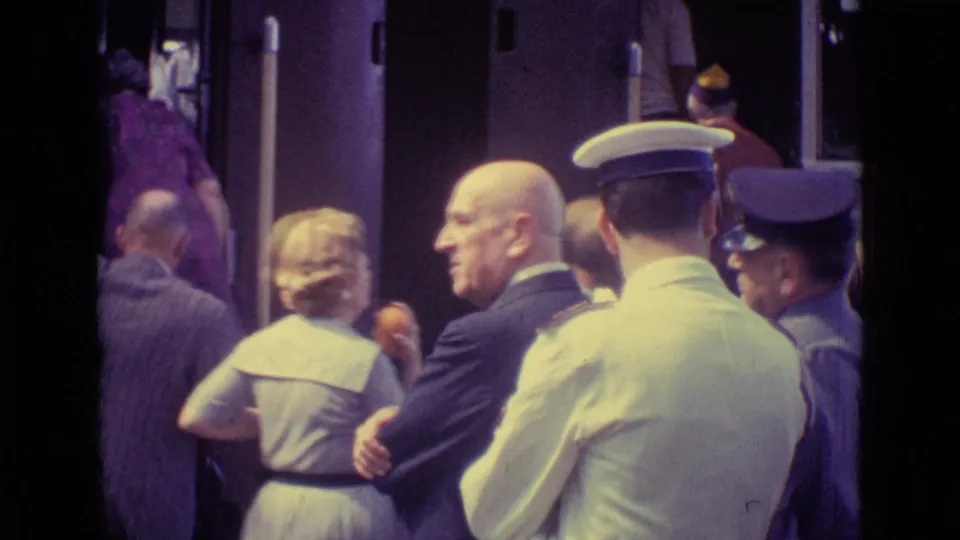 Adults in suits and dresses stand beside a train car in 1962 Venice as uniformed rail staff remain close to the door.