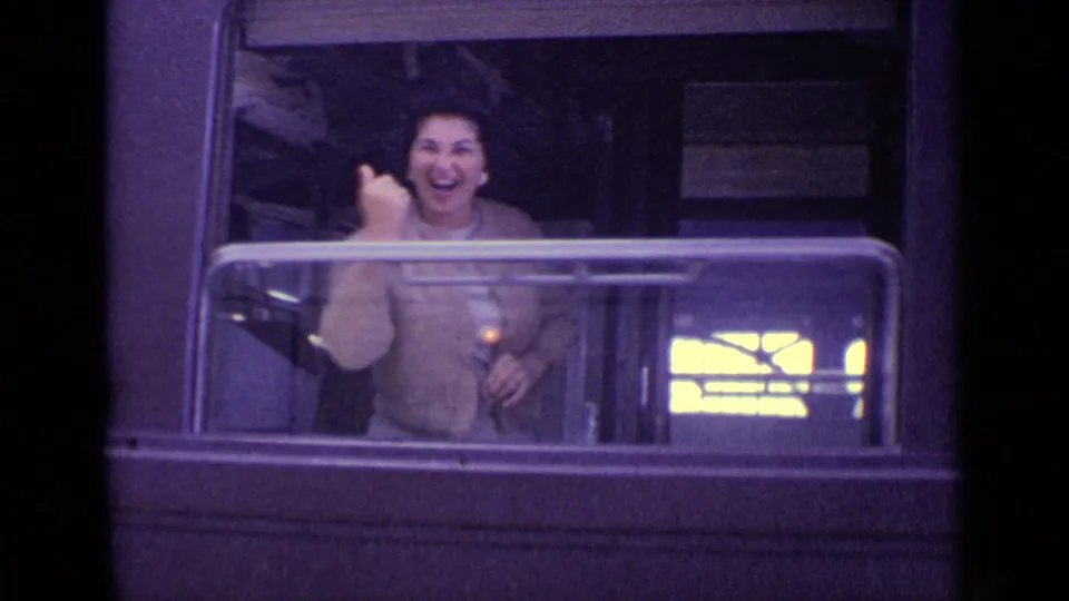A woman in a light sweater smiles and waves from a train window in this 1962 Venice home-movie frame.