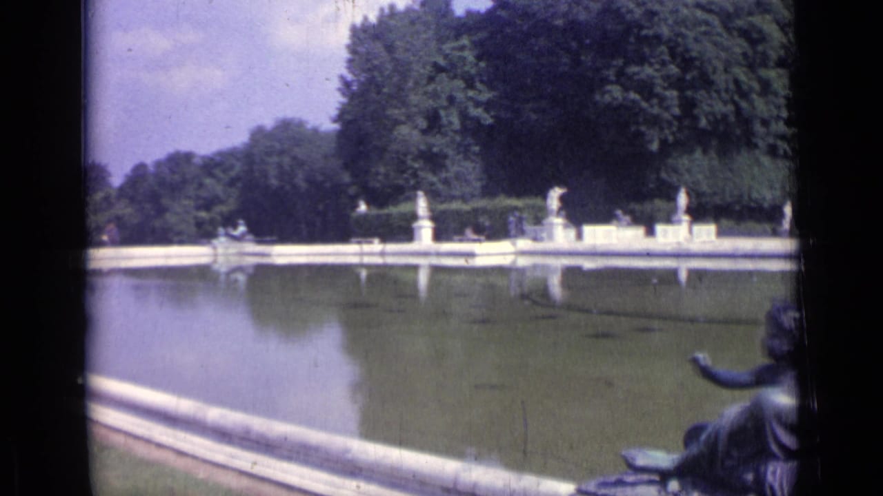 Long pool bordered by statues and trees, with a partial sculpture at the right edge.