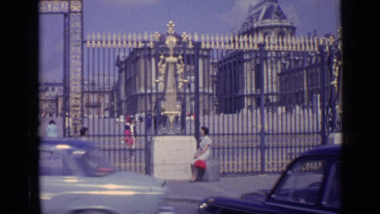 Versailles palace gates with tourists nearby and a light car passing in front.
