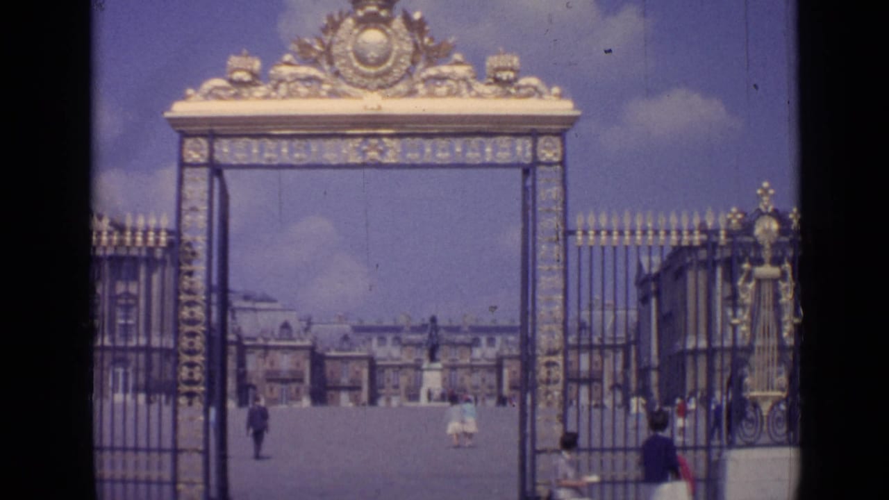 Ornate Versailles gate frames the distant palace with a few tourists in the courtyard.