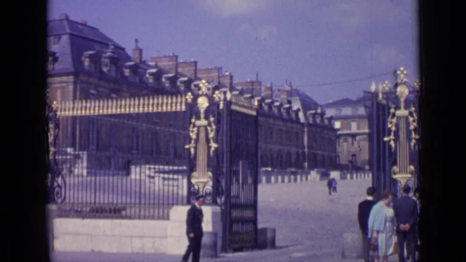 The Versailles entrance gate and palace buildings appear behind visitors gathered near the right side of the frame.