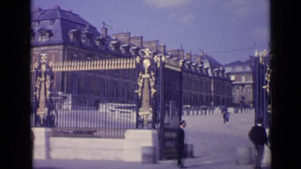 A wider 8mm frame shows the open Versailles gate, a guard near the entrance, visitors, and the palace facade beyond.