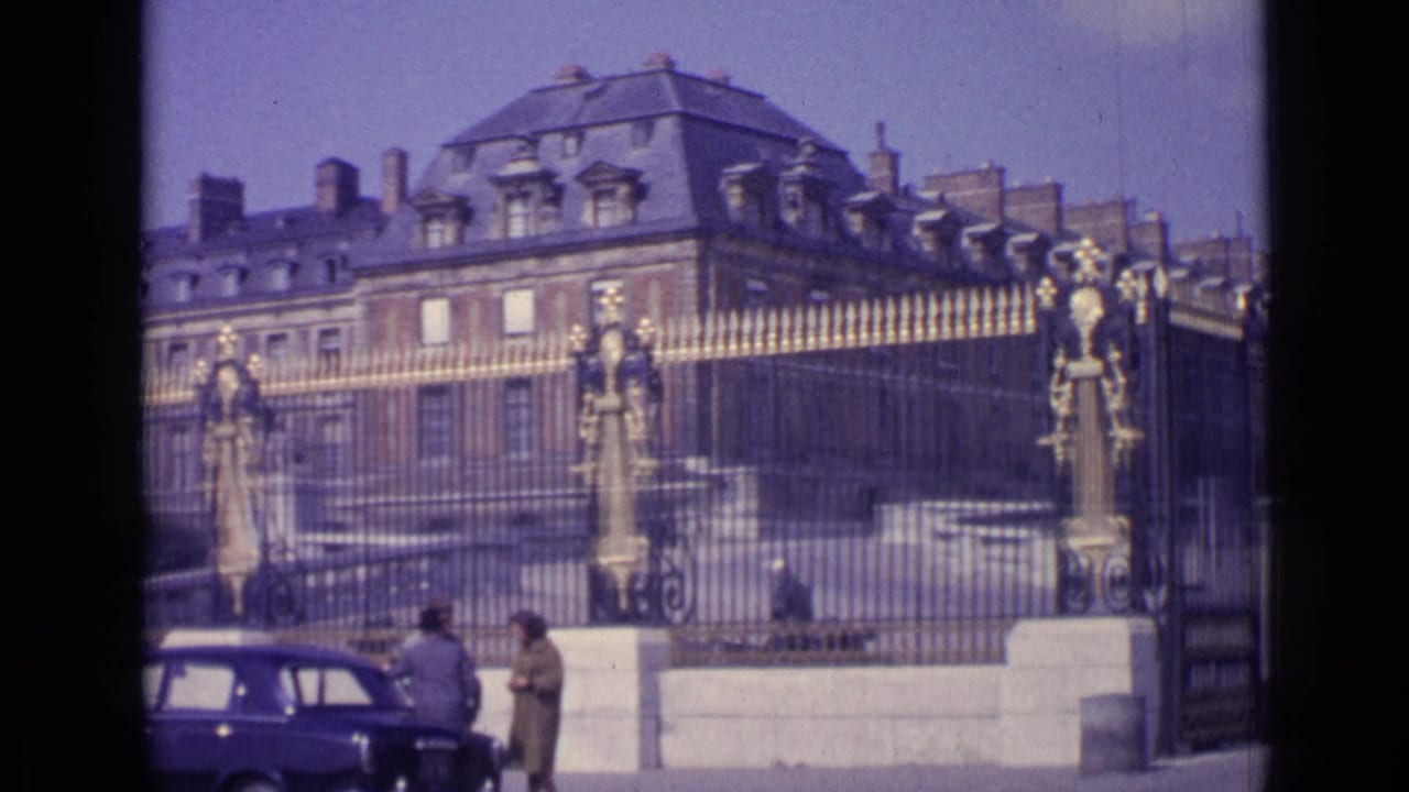 Palace facade and ornate gates with a dark car and pedestrians in front.
