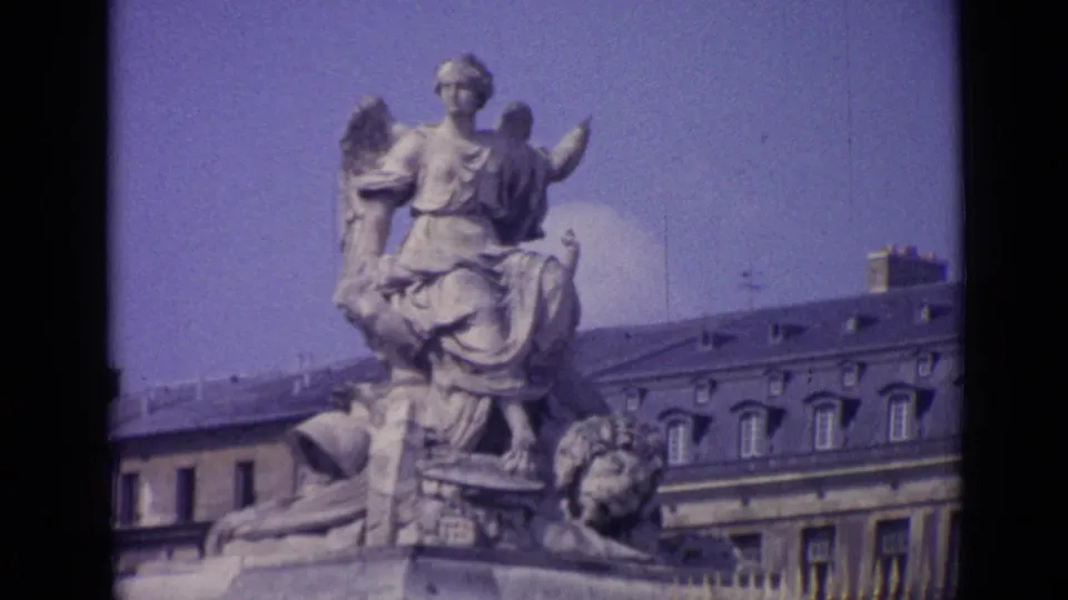 Wider 1962 Versailles view of a seated allegorical sculpture with palace windows, roofline, chimneys, railing, and blue sky.