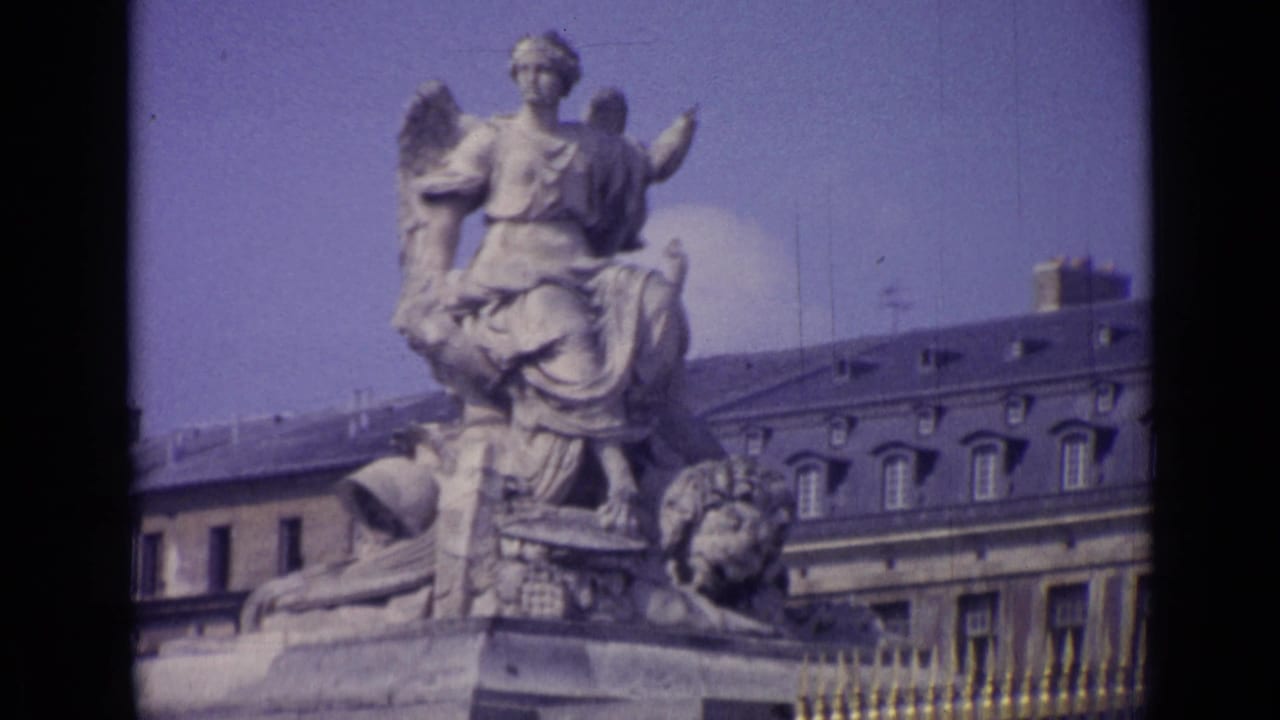 Stone monument with a seated winged figure above a formal building and ironwork.