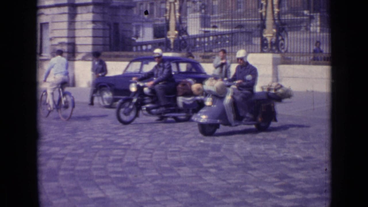 Motorcyclists and a scooter pass cyclists and pedestrians on a cobblestone street.