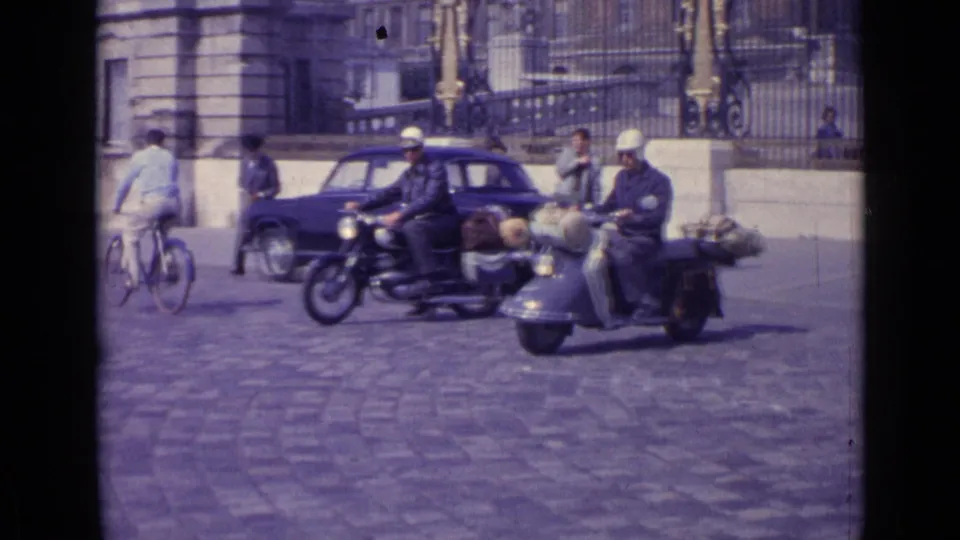 Motorcyclists, a loaded scooter, cyclists, pedestrians, and a compact car move through a Versailles cobblestone square in 1962.