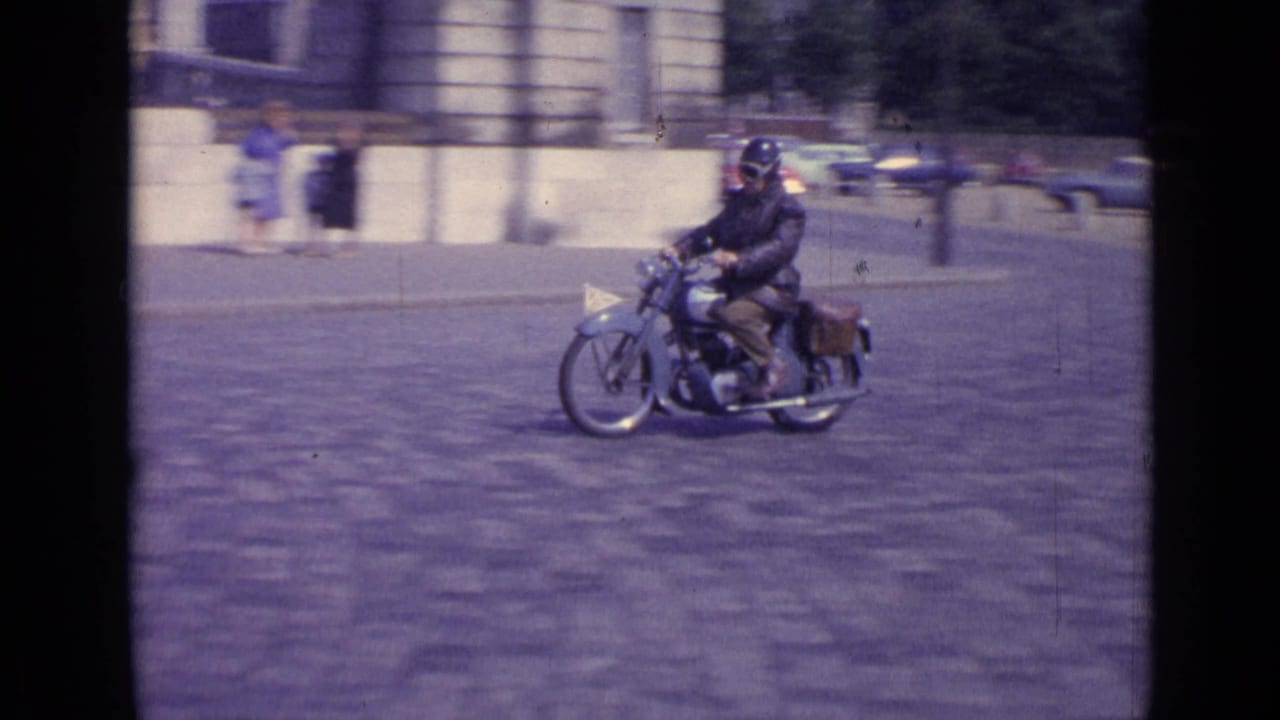 Motorcyclist riding across a cobblestone street near stone buildings.