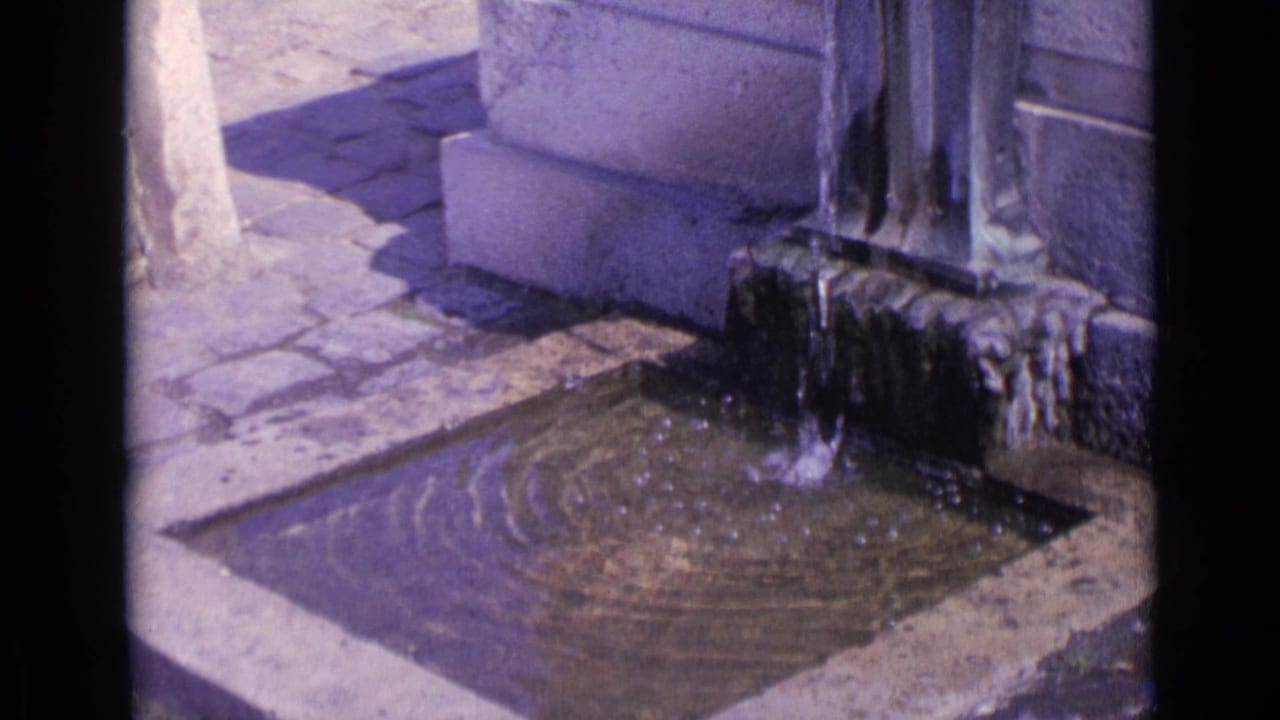 Water pours from a stone fountain into a square basin with ripples on the surface.