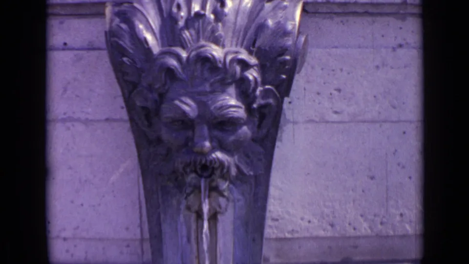 1962 Versailles close-up of a carved fountain mask with water flowing from the mouth against a stone wall.