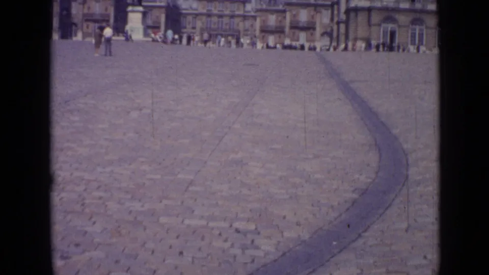 Wide 1962 Versailles square view with cobblestone paving, a curved border, distant classical facades, and a few pedestrians.