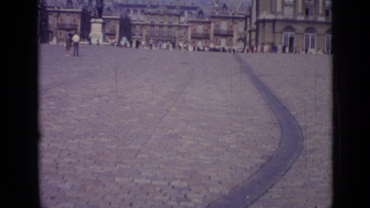 Wide cobblestone courtyard with palace buildings and distant visitors under a bright sky.