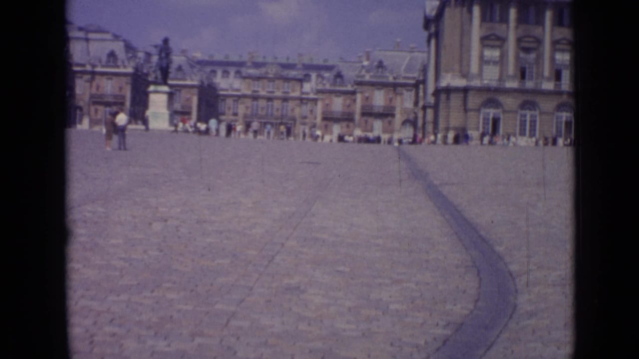 Wide palace courtyard with tourists scattered near the building line and a curved dark seam across the stones.