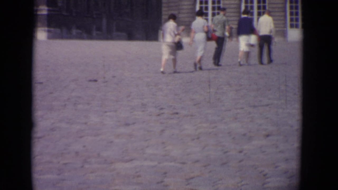 Five adults walk across a broad cobblestone courtyard toward a building facade.