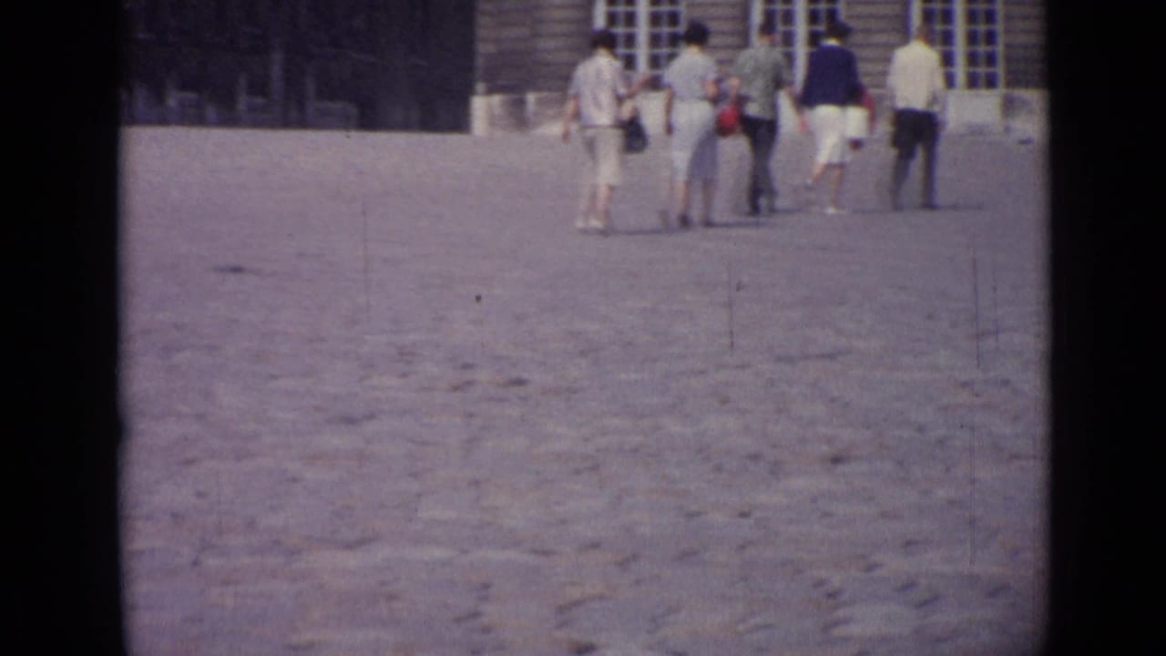 A small group of adults continues across the courtyard near a building with windows.