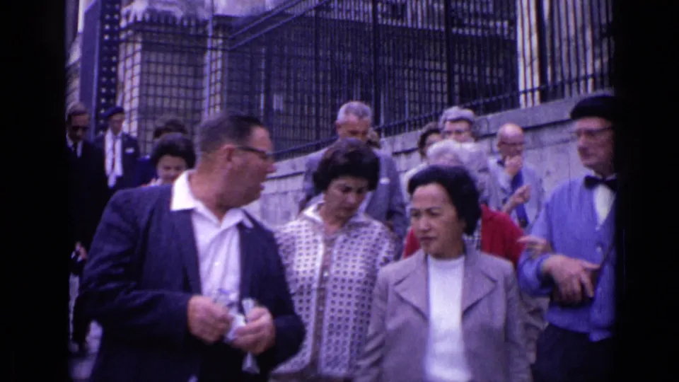 Adult visitors crowd a stone staircase beside a wrought-iron fence in Versailles, captured in soft 1962 8mm footage.