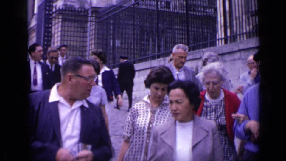 The Versailles staircase scene shows adult visitors passing close to the camera, with faces, coats, and a wrought-iron fence visible.