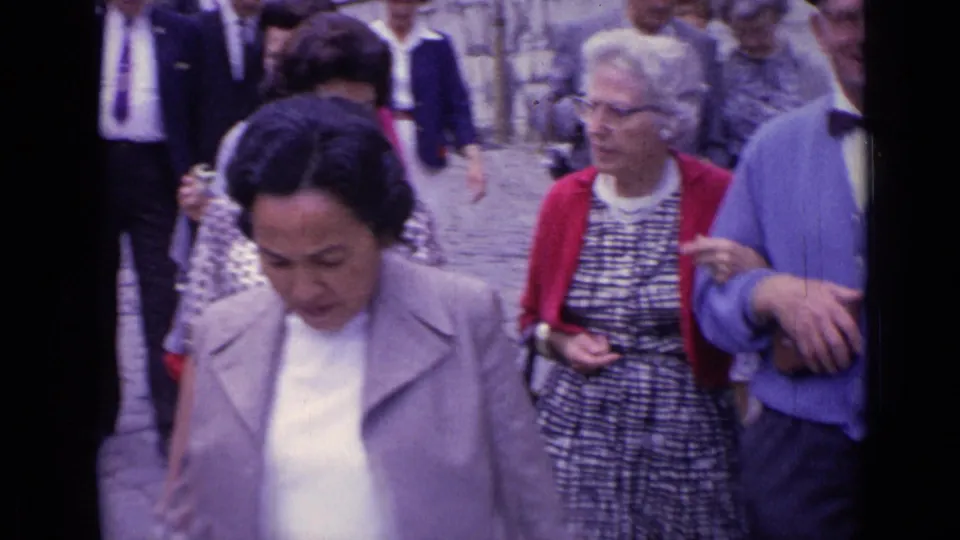 Close 1962 Versailles home-movie view of adult tourists walking past, with cardigans, patterned dresses, and handheld framing.
